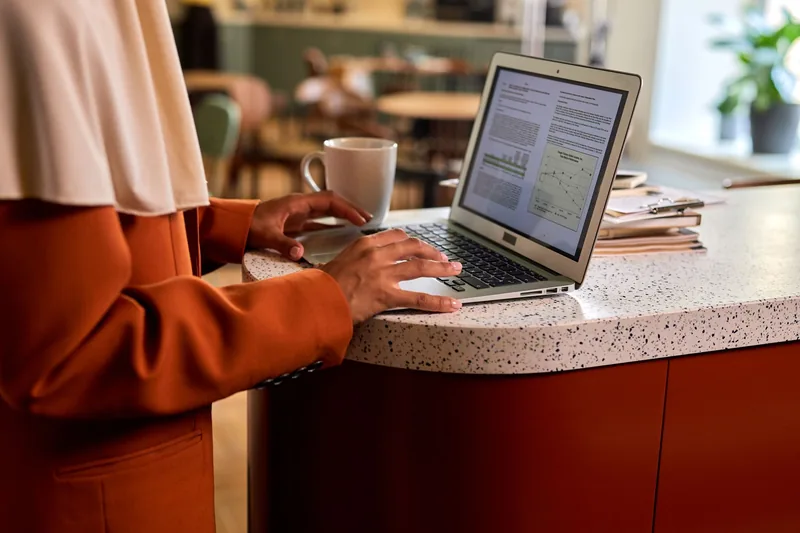 Business owner typing on a laptop at a cafe counter, writing up documents