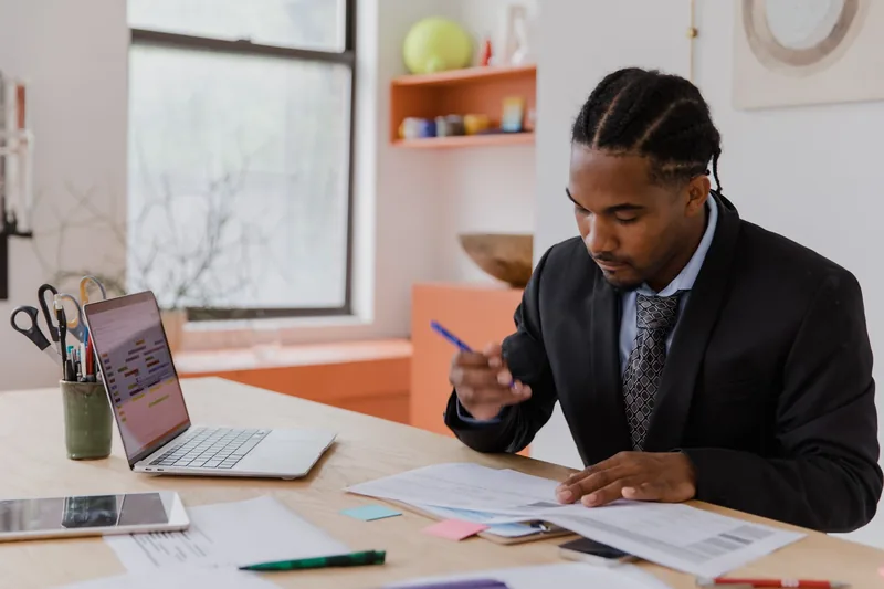Business owner reviewing printed reports with a pen next to an open laptop