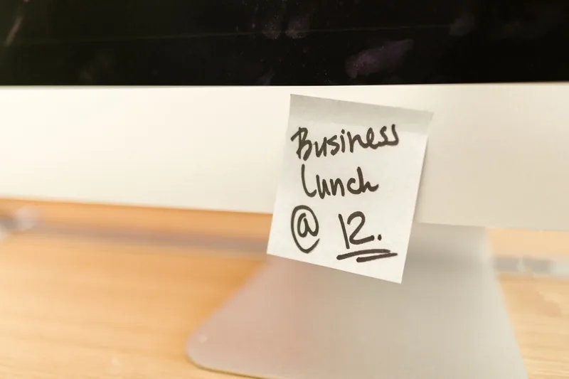 Handwritten sticky note reminder stuck to the bottom of a computer monitor
