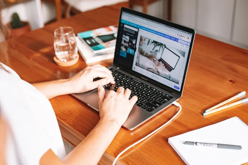 Person writing a blog article on a laptop at a wooden desk