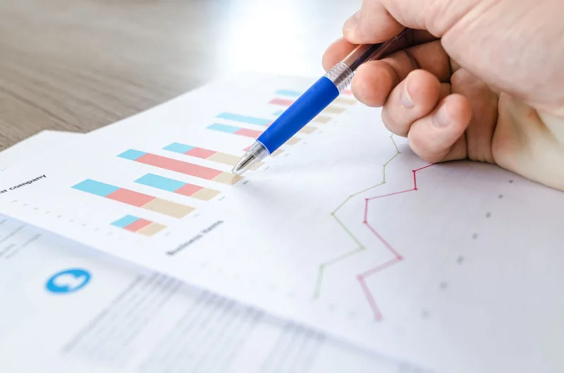 Hand holding a pen over printed bar and line charts on a business report