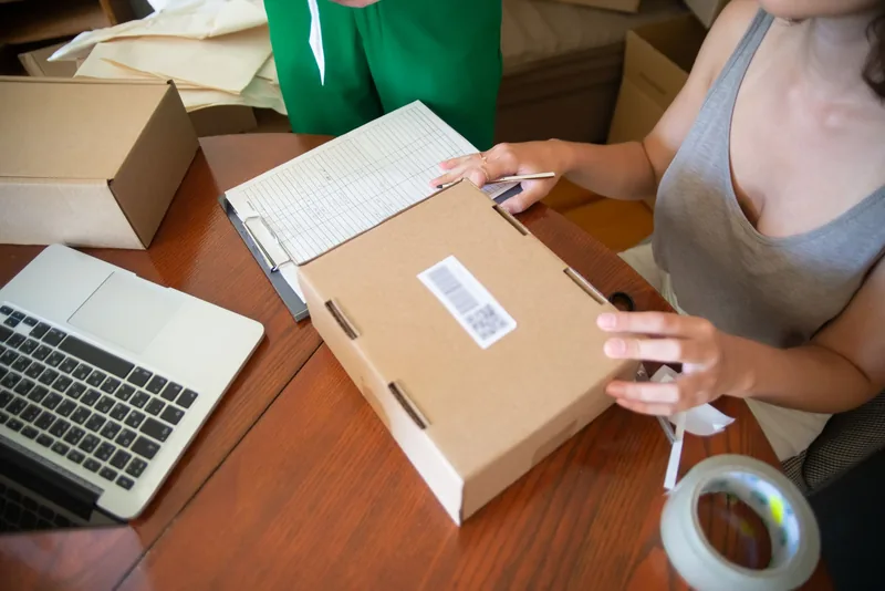 Small business owner packing an online order into a shipping box next to a laptop