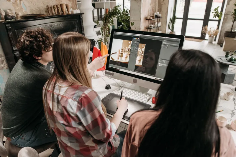 Three people at a desktop computer reviewing a product photo in an image editor