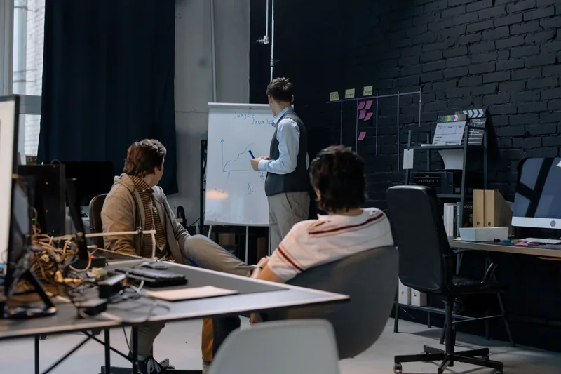 Small team in an office watching a colleague sketch a growth chart on a whiteboard
