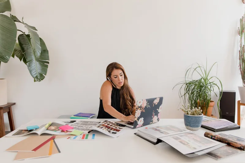 Small business owner working at a desk with a laptop, on the phone while reviewing paperwork