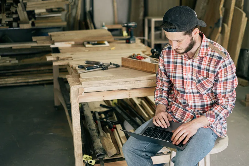 Woodworker sitting in his shop checking results on a laptop