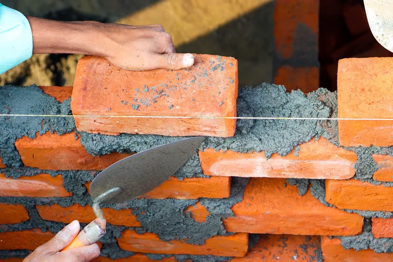 Close-up of a bricklayer setting a brick on fresh mortar along a level string line