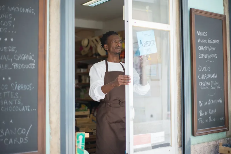 Shop owner in an apron opening the glass door of his small storefront in the morning