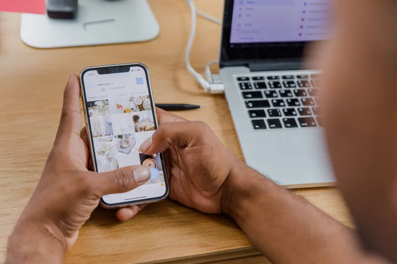 Person reviewing their Instagram profile grid on a phone at a desk with a laptop