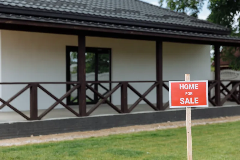 Home for sale sign on a wooden post in front of a suburban house