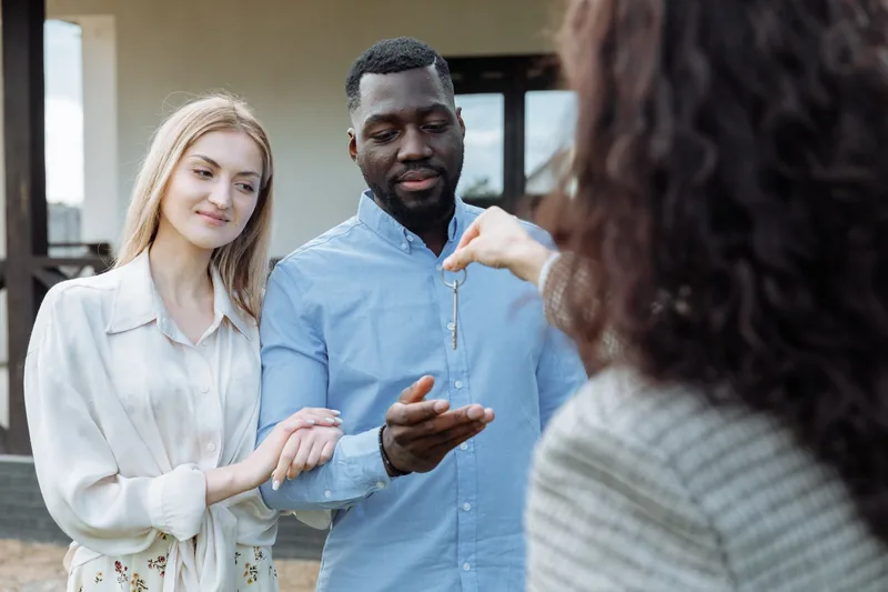 Real estate agent handing house keys to a happy couple outside their new home