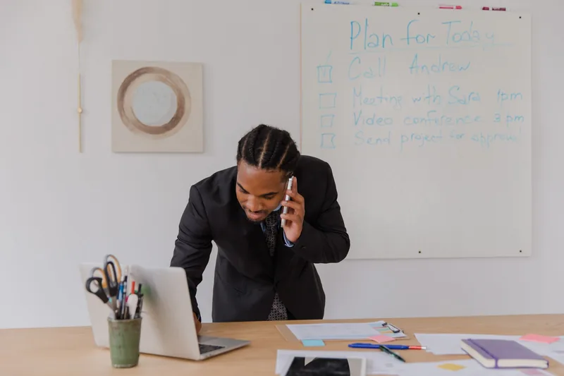 Business owner taking a phone call while checking his laptop at the office