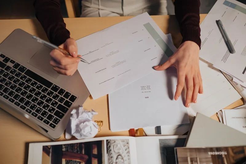 Person reviewing printed reports with a pen beside a laptop