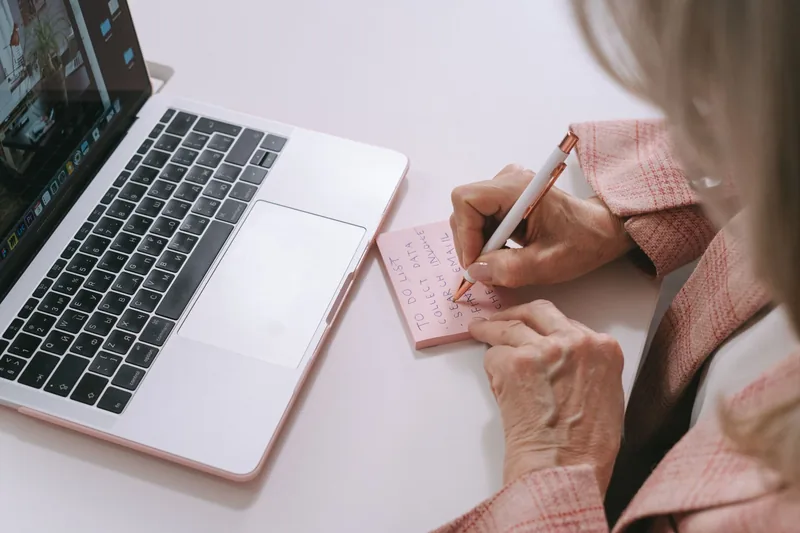 Business owner writing a prioritized to-do list beside a laptop
