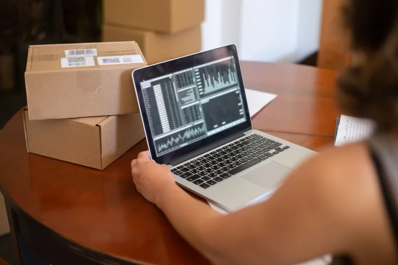 Small business owner reviewing analytics charts on a laptop beside shipping boxes
