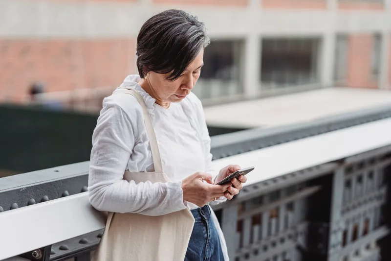 Woman leaning on a railing while filling something out on her smartphone