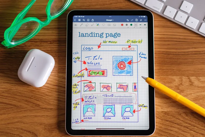 Hand-drawn landing page wireframe on a tablet showing a headline, call-to-action button, image row and testimonials