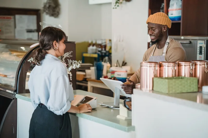 Cafe owner in an apron smiling while ringing up a customer at the counter