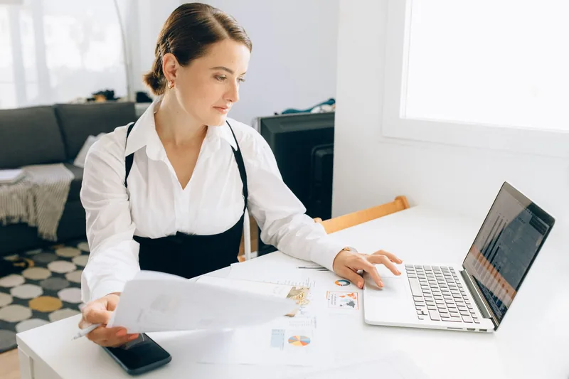 Business owner at a bright desk reviewing a printed report next to her laptop