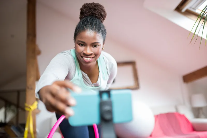 Trainer filming a short workout video on a phone mounted on a tripod at home
