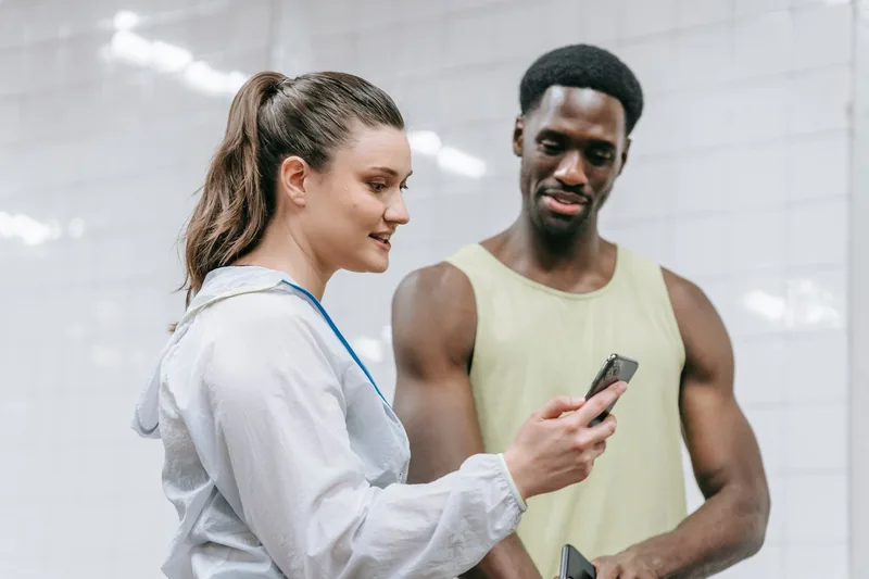 Personal trainer showing a client a booking screen on her phone in a gym