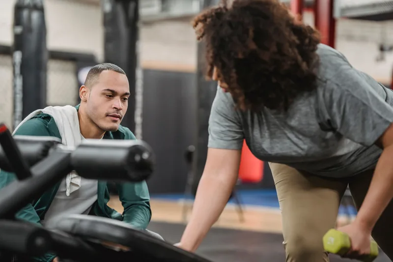 Personal trainer coaching a client through a dumbbell exercise on a gym floor