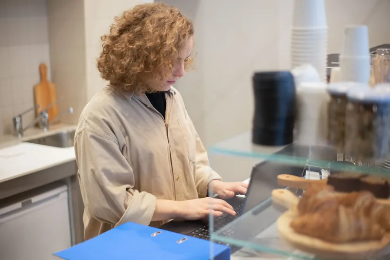 Cafe owner working on a laptop behind the counter, managing her own ad campaigns