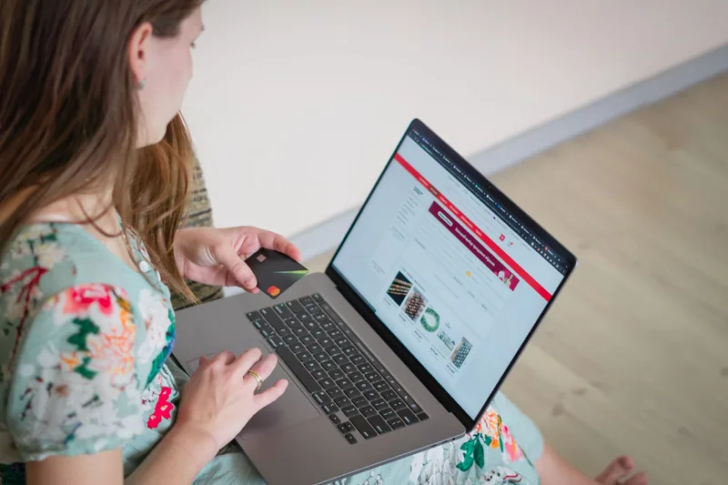 Woman shopping on a laptop at home holding a credit card mid-checkout