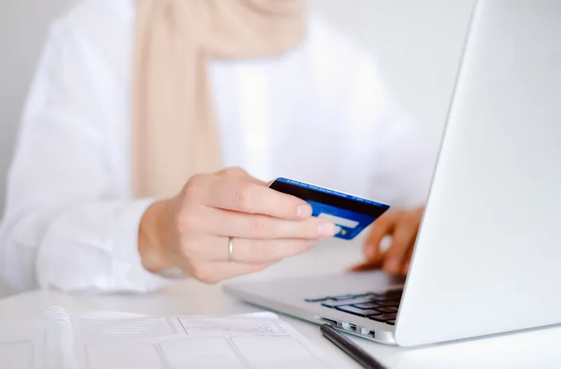 Person holding a credit card while shopping on a laptop at a desk