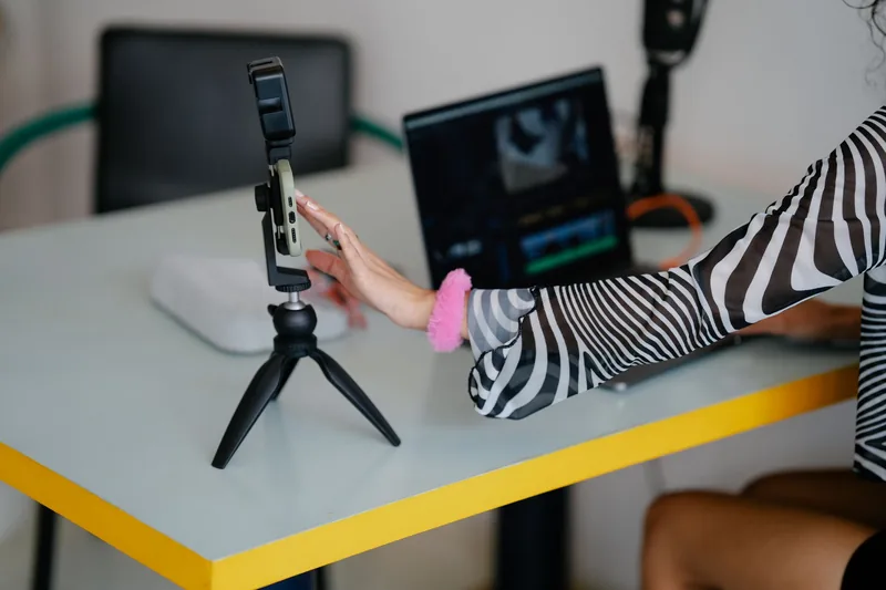 Creator editing a phone-recorded clip on a laptop next to a smartphone mounted on a tripod