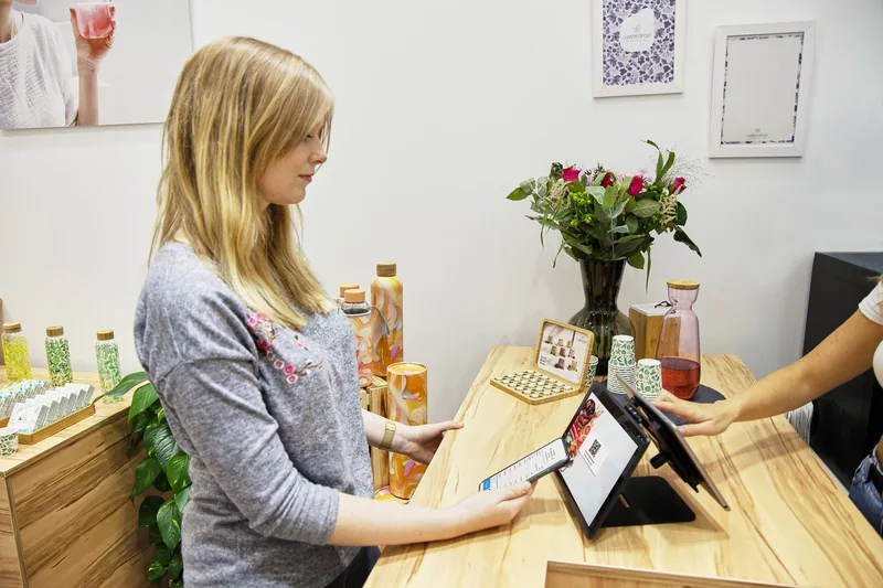 Customer at a shop counter holding a phone next to a point-of-sale terminal