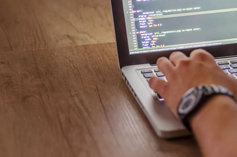 Hands typing on a laptop showing website source code on screen
