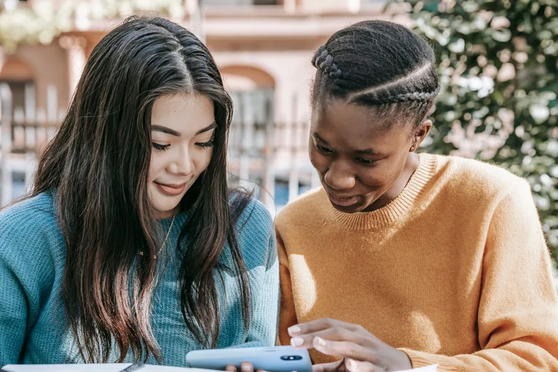 Two young women watching a video together on a smartphone outdoors