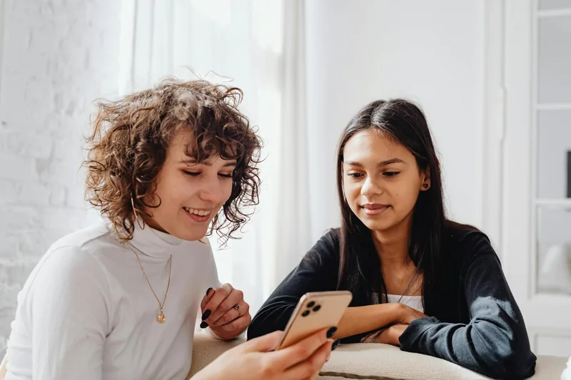 Two friends smiling at a phone together, sharing a recommendation