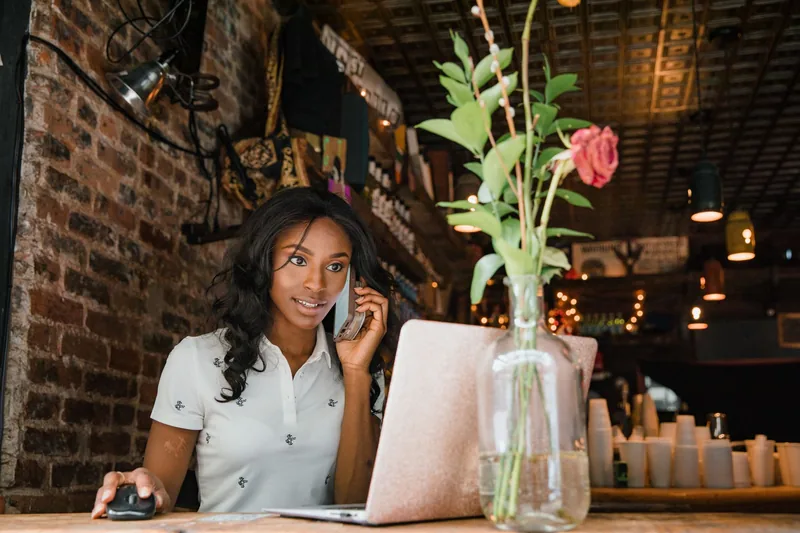Woman at a cafe counter on a phone call while working on her laptop