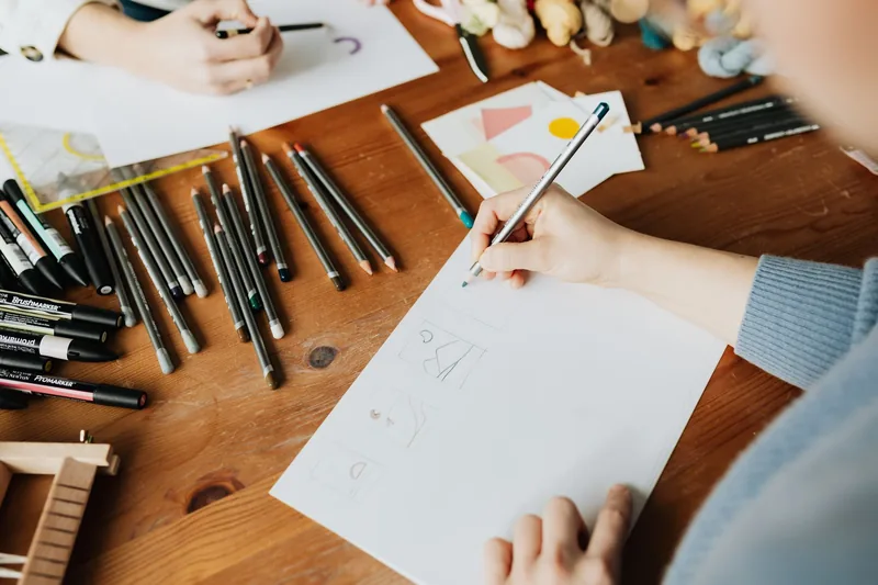 Designer sketching page layout ideas on paper surrounded by pencils and markers