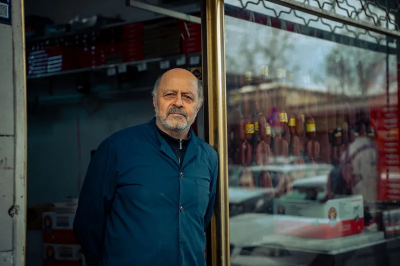 Shop owner in a blue work jacket standing in the doorway of his store